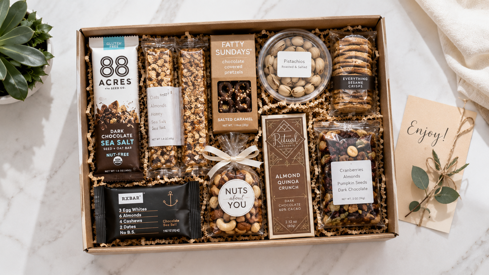 A neatly arranged gourmet snack box with granola bars, nuts, chocolates, and healthy treats, shot from above